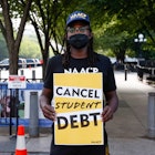 A protestor with a mask on and a hat holds a sign that says "Cancel Student Debt"
