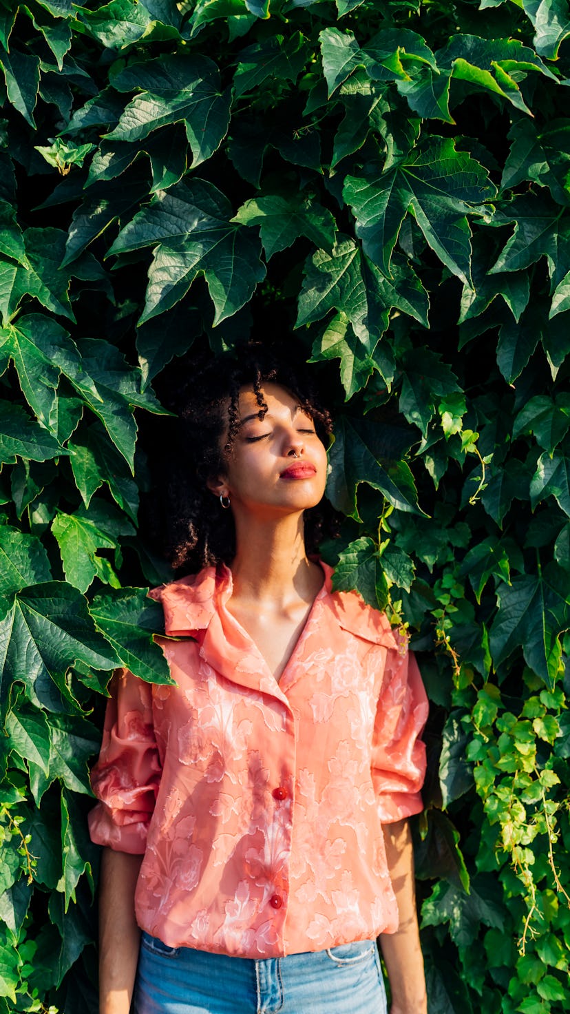 Young woman closing her eyes in front of a plant backdrop. Uranus retrograde arrives on Aug. 24 in h...