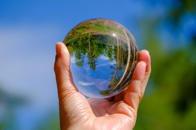 Hand holding glass sphere which is reflecting an upside down image of a forest. 
