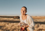Woman with short hair looking at camera and laughing loudly holds vintage camera at sunset. She is w...