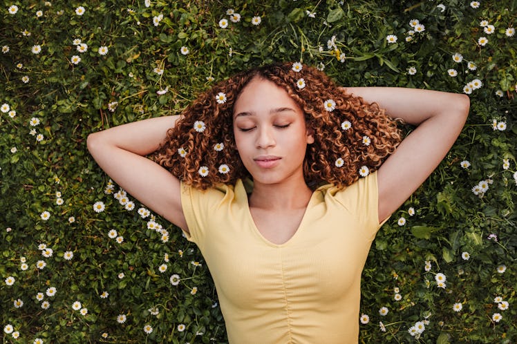 young woman lays in a field of flowers as she thinks about the spiritual meaning of the september 20...