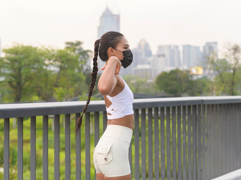 A brunette woman with braided hair in a white top and off-white shorts with a face mask at risk of g...