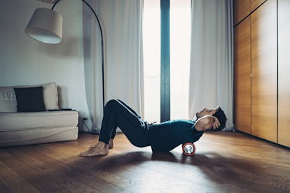 Die 6 besten Gleichgewichts- und Mobilitätsübungen für Männer, um flexibel zu bleiben 2 Junger Mann mit Schaumstoffrolle auf dem Rücken zu Hause.