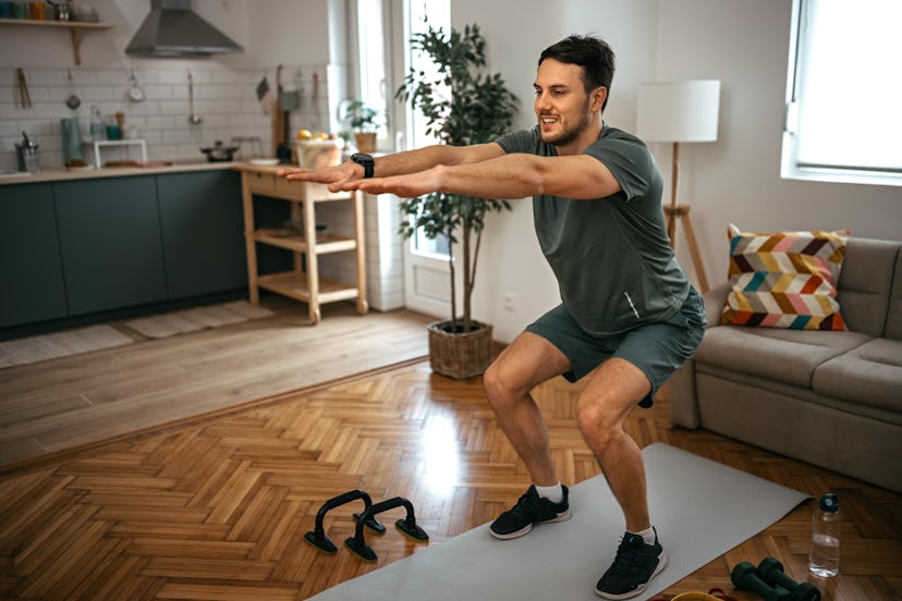A man doing squats on a yoga mat at home