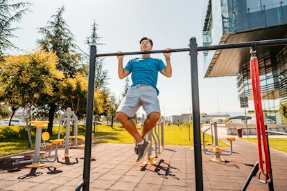 Bestes Körpergewichtstraining für Muskelaufbau 8 Ein Mann macht Klimmzüge an einer Stange im Freien in einem öffentlichen Park.