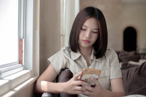 Happy Young Girl Sitting on a Cozy Sofa at a Cofee House while Texting on her Mobile Phone