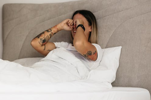 Beautiful young tattooed woman laying in bed in the morning. Beautiful woman with tattoos using her ...