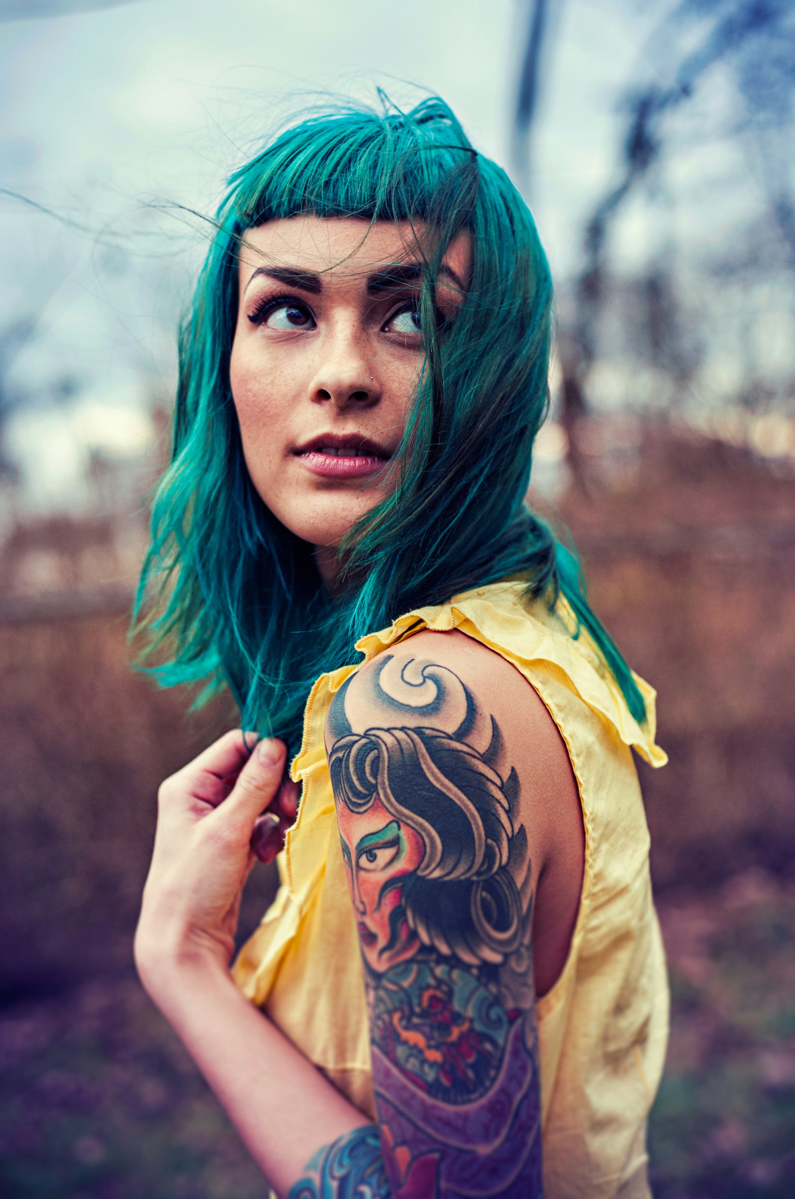 Tattooed model with blue hair posing for a photo in a yellow shirt