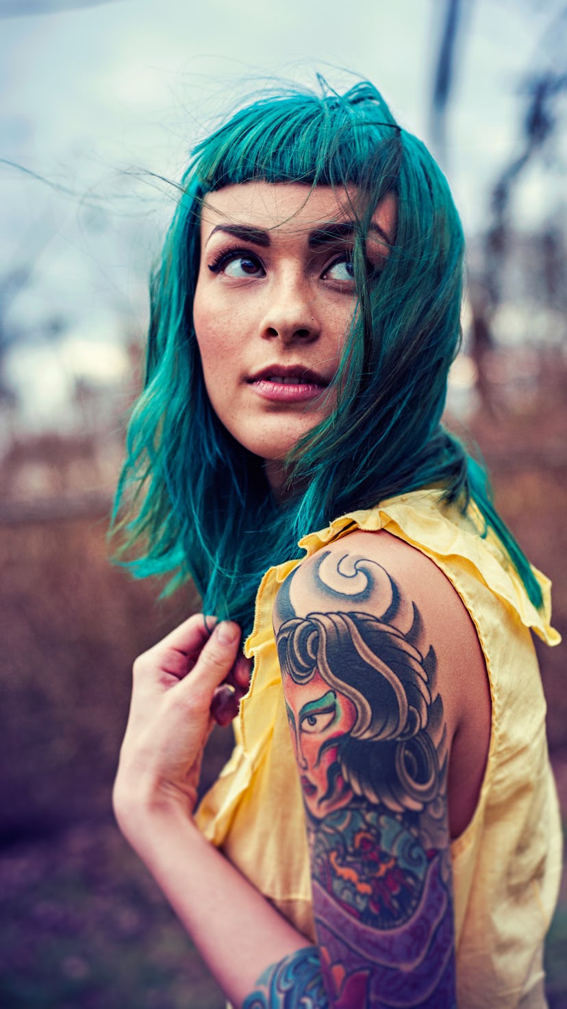 Tattooed model with blue hair posing for a photo in a yellow shirt