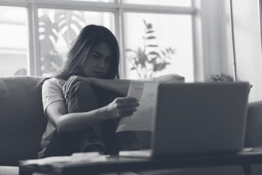 年轻的亚洲妇女正在经历财务问题,阅读发票纸或逾期的账单在她的哈…