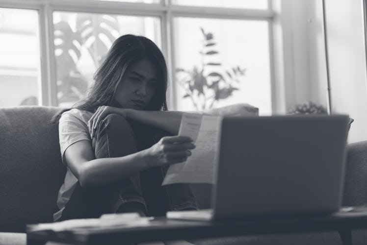 Young Asian woman going through financial problems, reading invoice paper or overdue bills in her ha...