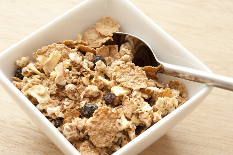 Tasty healthy muesli with dried fruit, raisins and nuts in a square dish with spoon, high angle clos...
