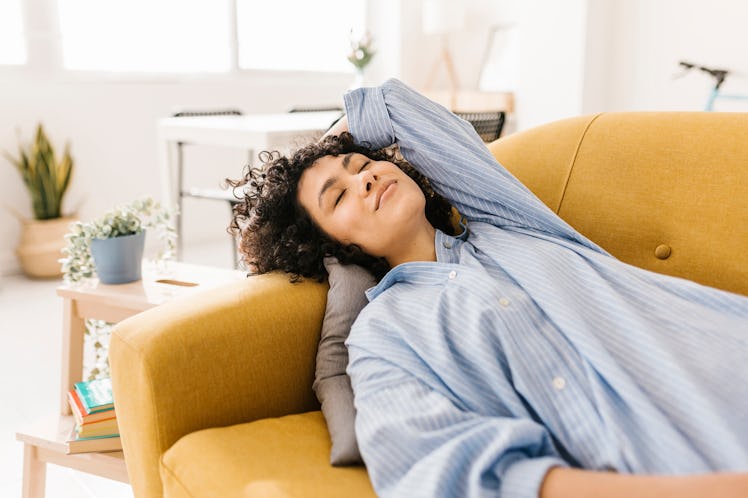 young woman leans back on couch cushion as she thinks about her sept. 5, 2022 weekly horoscope