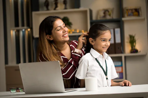 Working mother combing hair of her daughter in school uniform at home