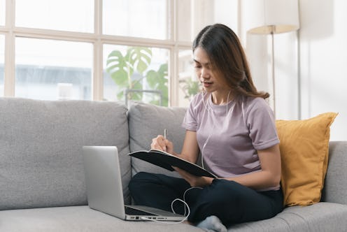Portrait of beautiful young Asian female sitting on sofa at home, watching webinar training or study...