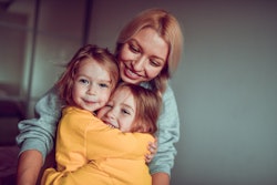 Smiling Mother Embracing twin daughters in a list of the best instagram captions for pictures of twi...