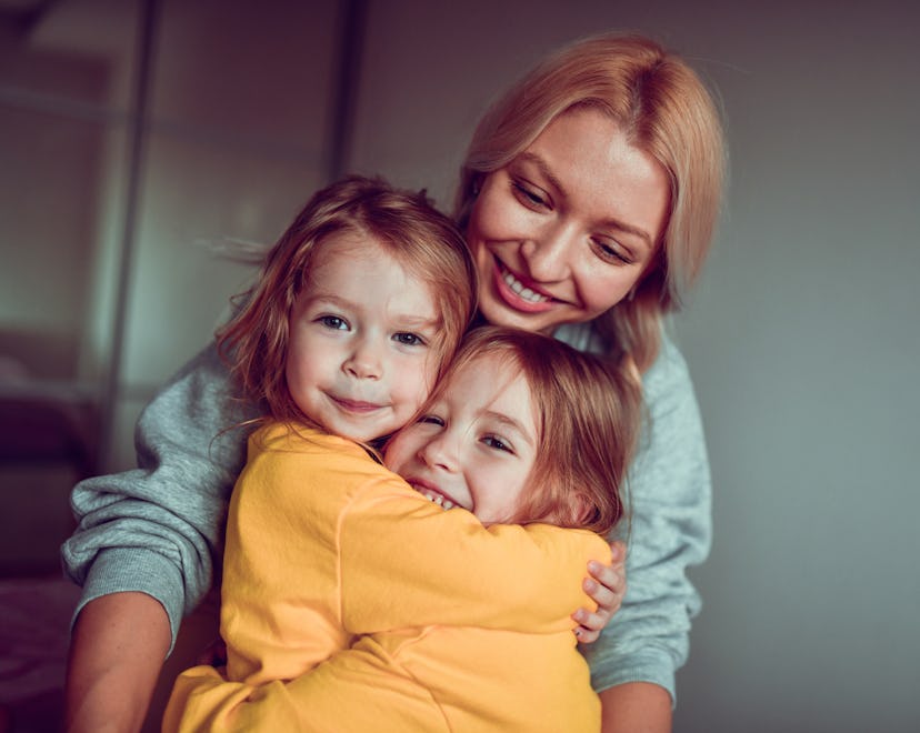 Smiling Mother Embracing twin daughters in a list of the best instagram captions for pictures of twi...