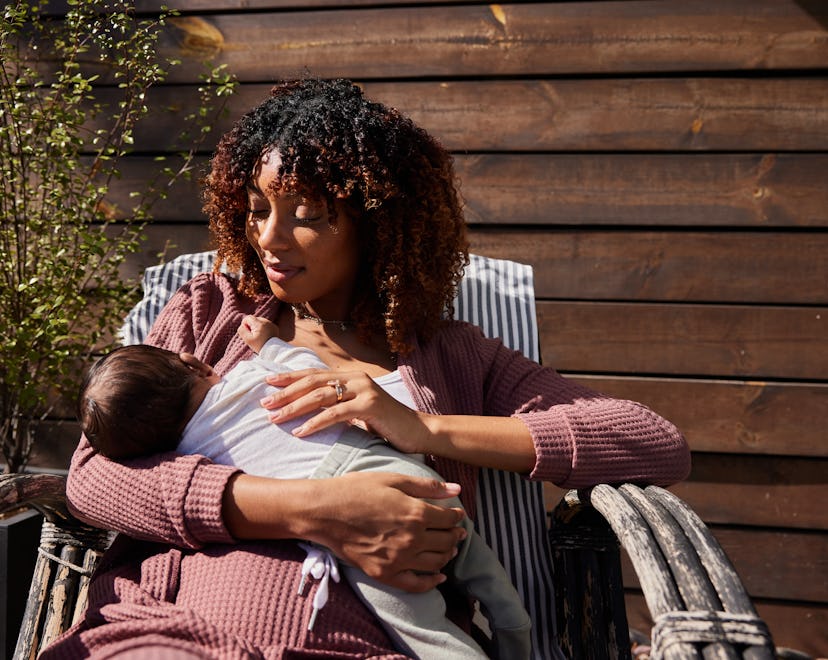 Mother looking down at her little baby boy and smiling while sitting outside on a deck chair on a su...