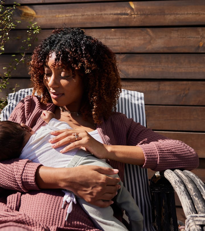 Mother looking down at her little baby boy and smiling while sitting outside on a deck chair on a su...