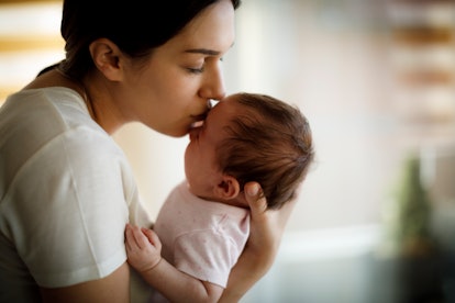 Mother kissing her crying baby in an article about how to help baby breathe with a cold