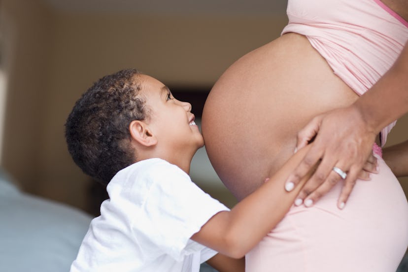 a child kissing their mom's pregnant belly in an article about creative ways to tell your partner yo...