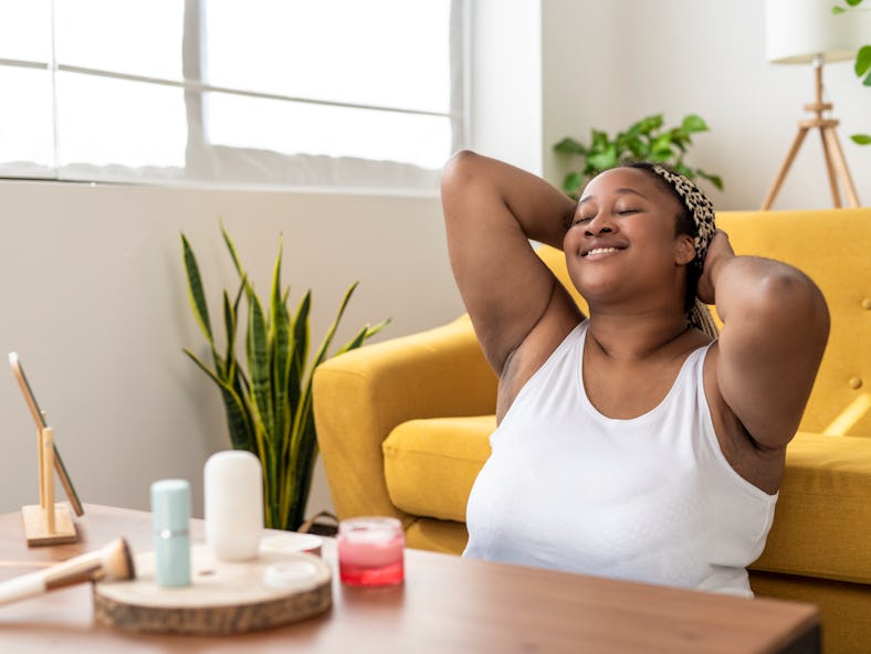 young woman smiles with her eyes closed as she lounges at home and reflects on how Mercury retrograd...