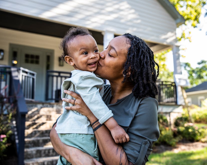 Mother holding toddler in front of new home in an article about Virgo baby boy names.
