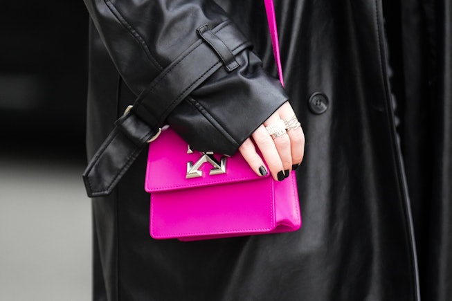PARIS, FRANCE - MARCH 03: A guest wears a black shiny leather long coat, silver rings, a neon pink s...
