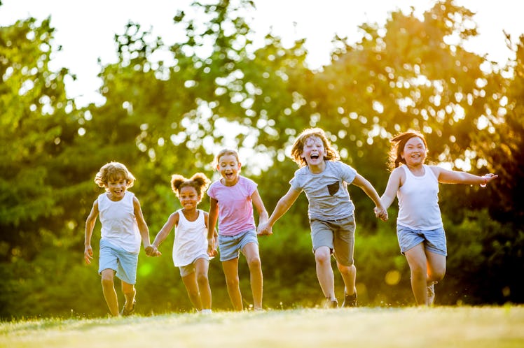 Children holding hands and running in park, laughing.
