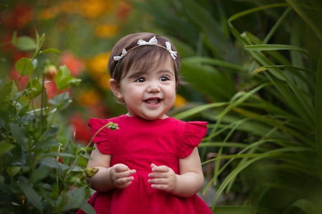 Cute baby girl smiling at camera surrounded by flowers in article about girl names that start with W