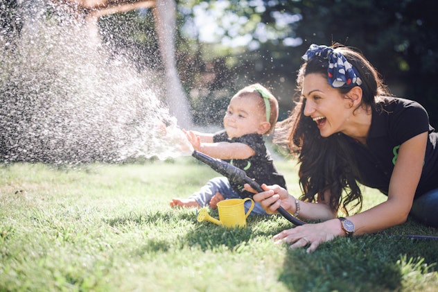 Happy mother having time together with his baby in garden, they playing with water in garden in arti...