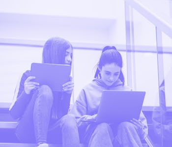 Girls on the high school stairs with laptop and tablet. Digital learning concept.
