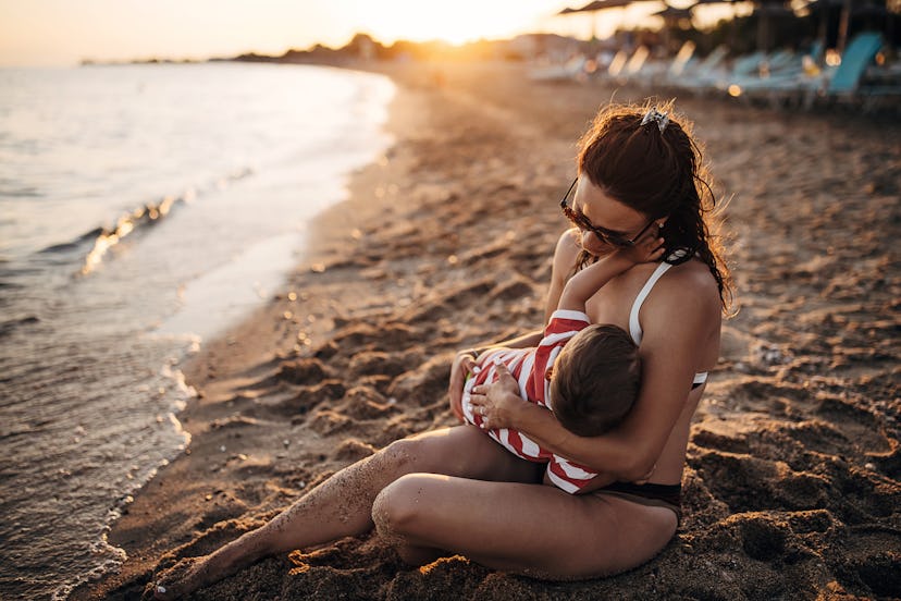Woman sitting on the beach and breast feeding her baby boy in an article about "what are the benefit...