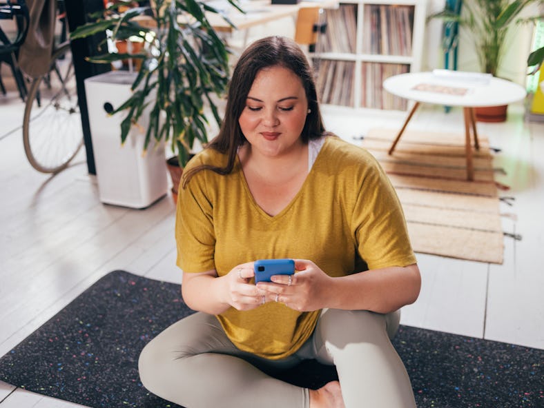 A woman sitting on her exercise mat looks up core Pilates workouts for abs that you can do at home o...