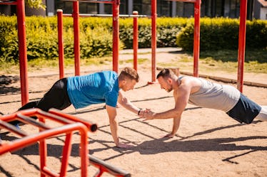 两个英俊的年轻人在户外一起做俯卧撑训练。