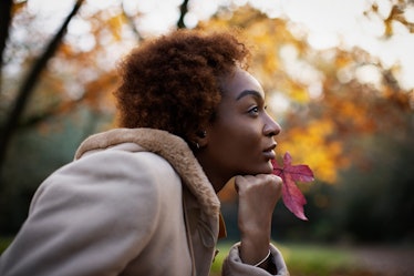 Young woman holding red autumn leaf and looking away in park after reading her October 2022 horoscop...