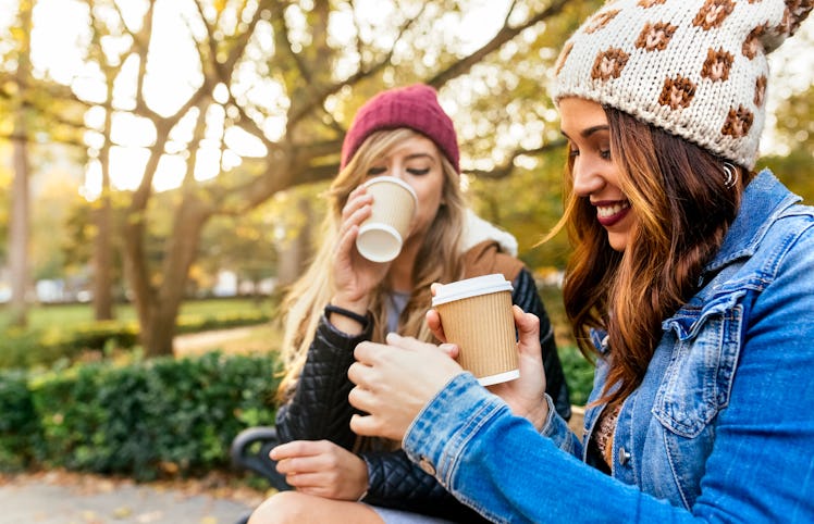 Two girls sitting in a park and drinking pumpkin spice latte