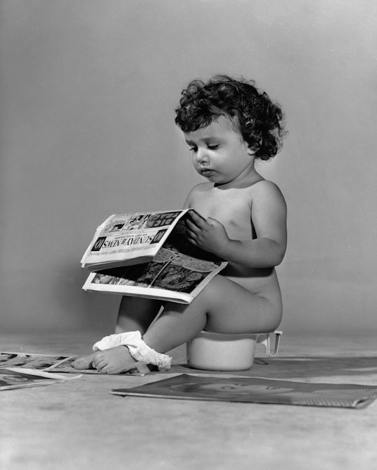 Infant sitting on a potty reading the newspaper. (Photo by Camerique via Getty Images)
