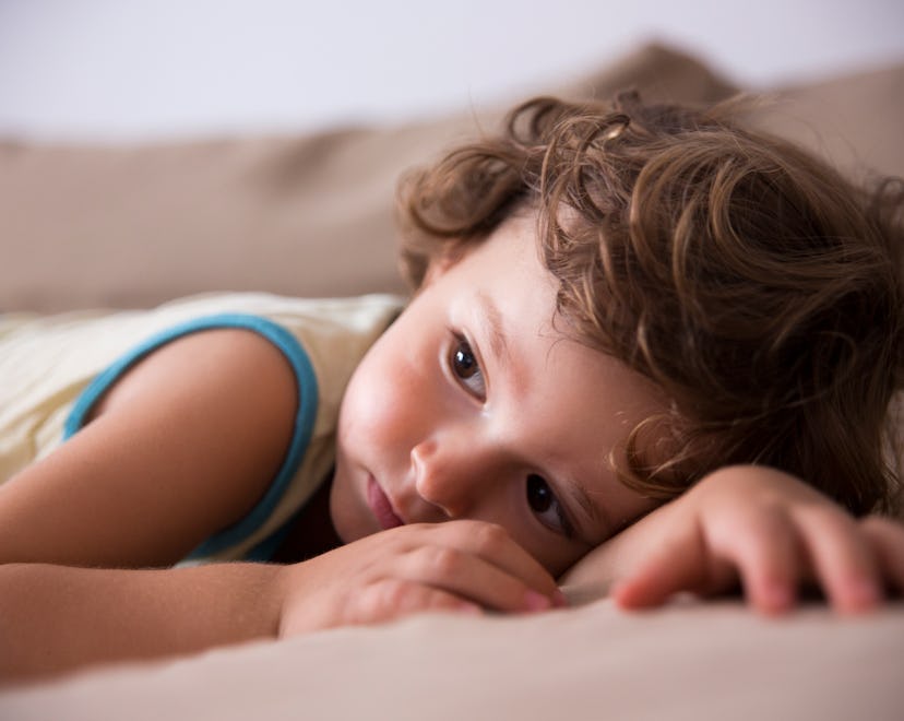 Child lit by diffused lighting, laying on the couch looking off into the distance.