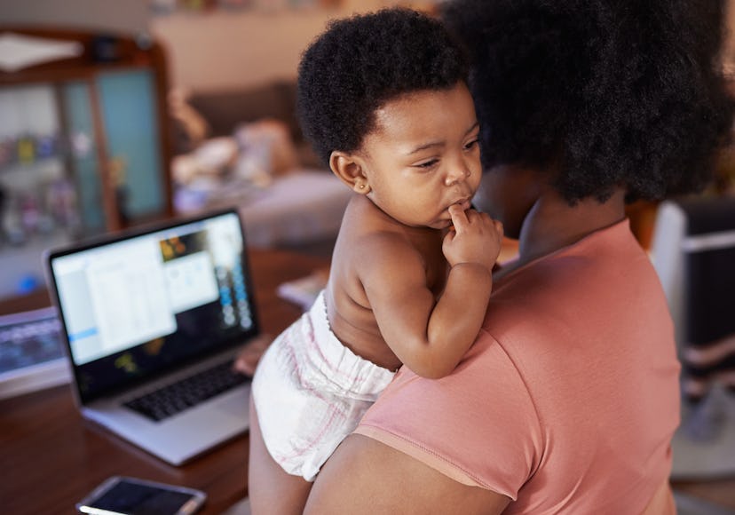a mom snuggles her baby as she looks something up on a computer. 