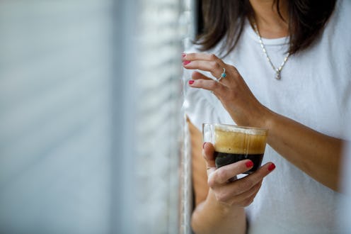 Close up shot of unrecognizable woman enjoying a cup of coffee by the window, peeking outside throug...