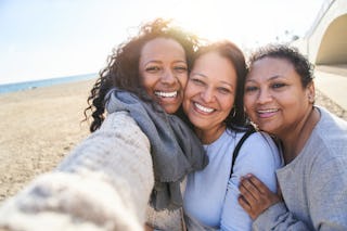 A smiley photo of a family of three women taking a selfie of themselves, looking at camera and with ...