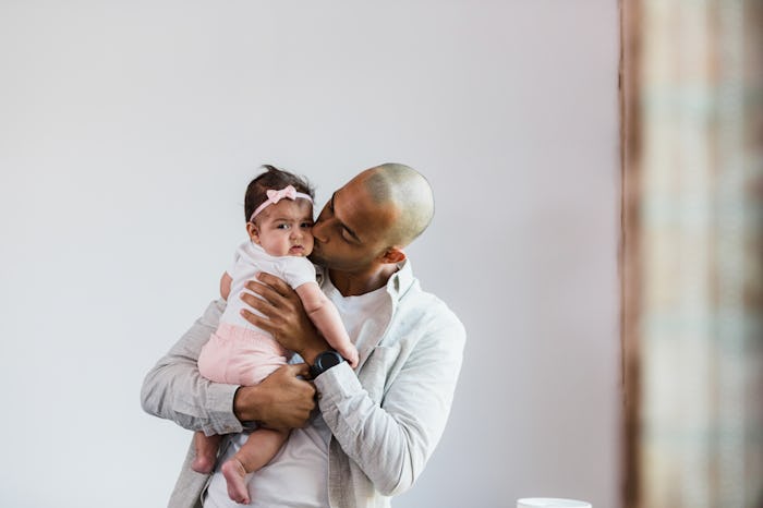 As the baby girl looks at the camera, the mid adult father kisses her on the cheek in article about ...