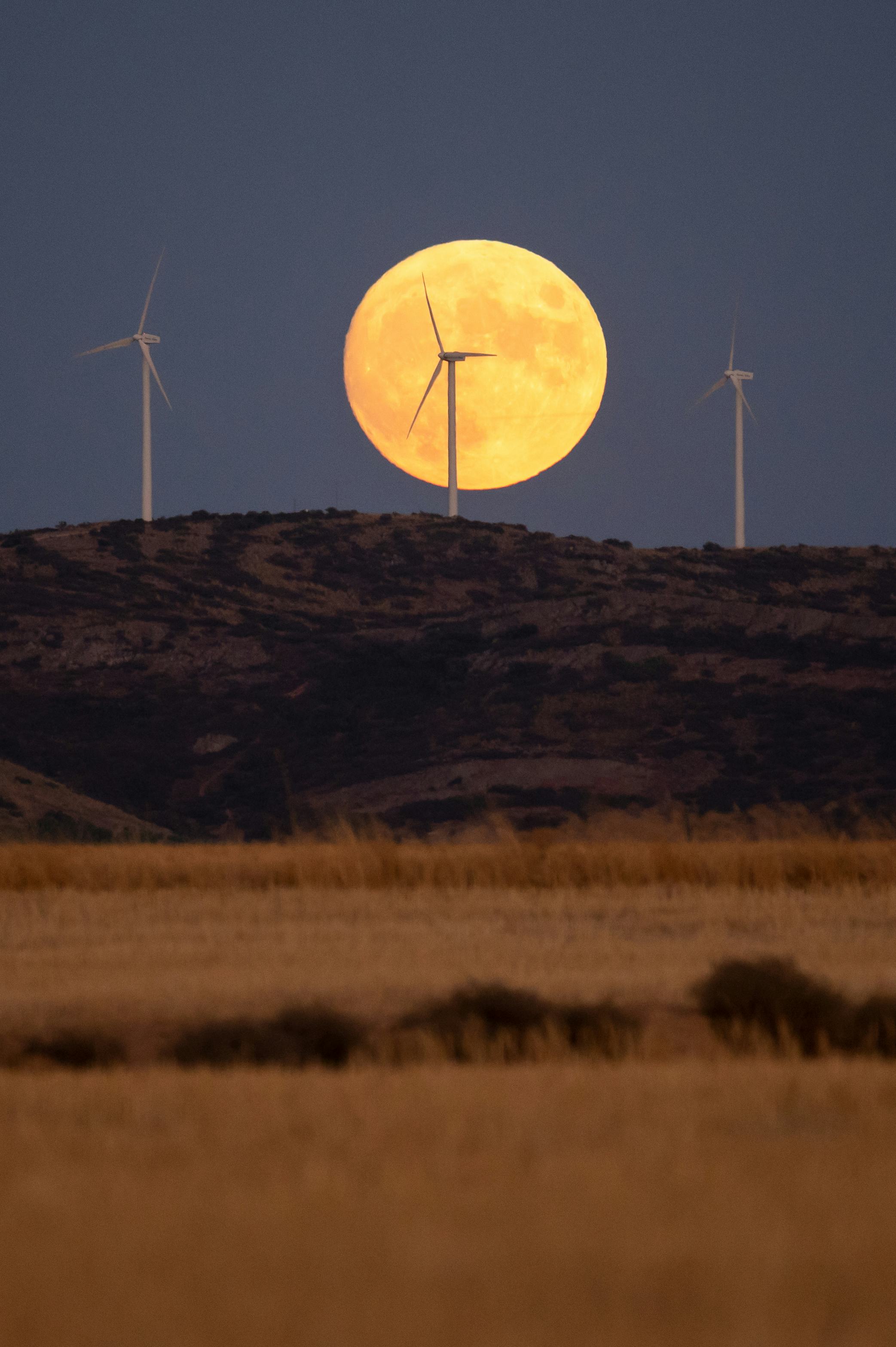 TOLEDO, SPAIN - 2022/09/09: The full Harvest Moon rises over wind turbines of a wind farm with a rec...