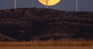 TOLEDO, SPAIN - 2022/09/09: The full Harvest Moon rises over wind turbines of a wind farm with a rec...