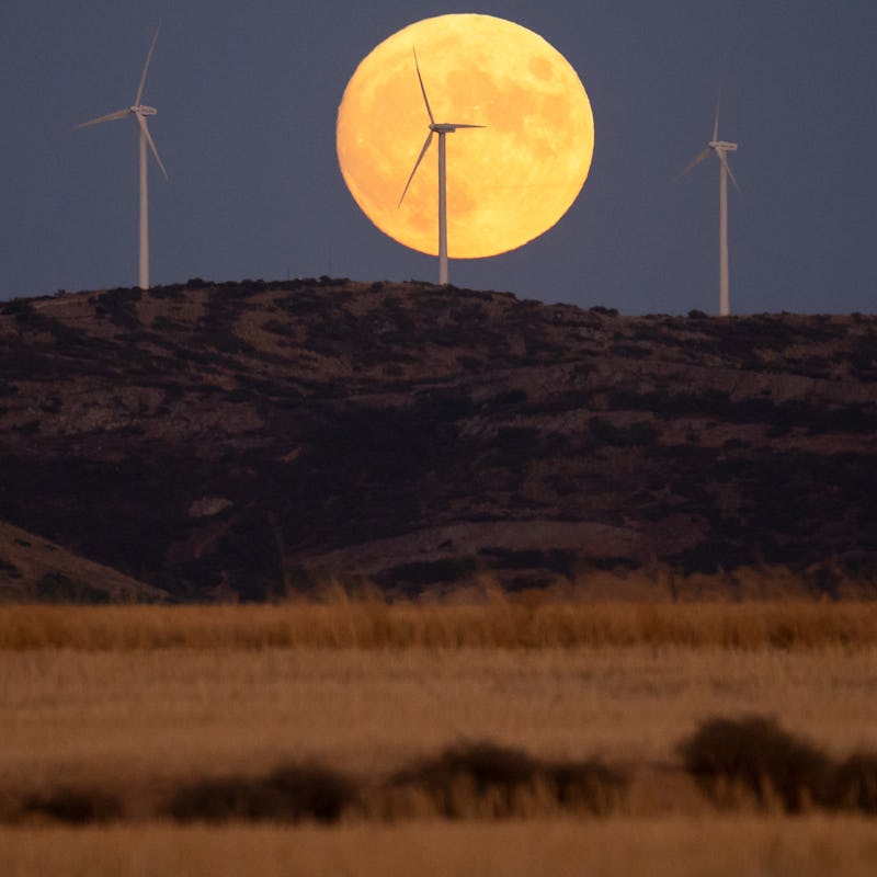 TOLEDO, SPAIN - 2022/09/09: The full Harvest Moon rises over wind turbines of a wind farm with a rec...
