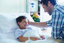 Loving father looking at ill son in bed at hospital ward
