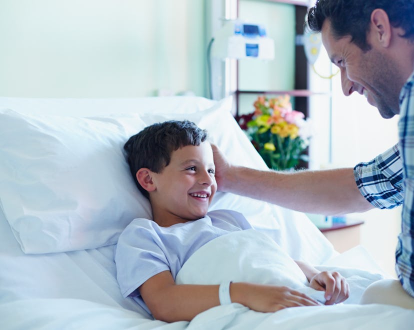 Loving father looking at ill son in bed at hospital ward
