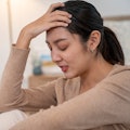 Asian woman sitting on floor next to bed feeling depressed