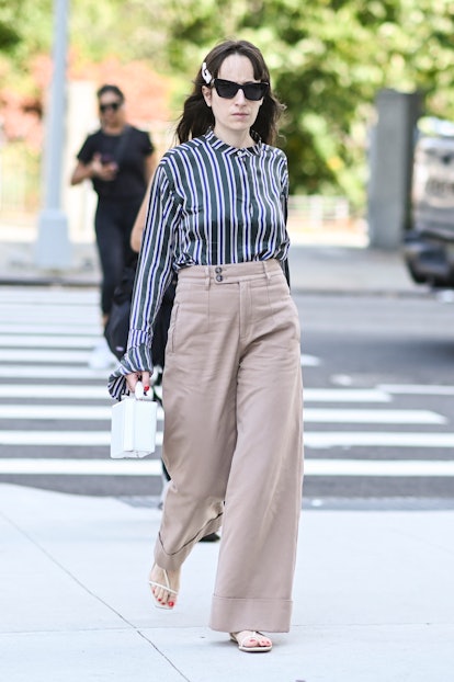  A guest is seen wearing a white and blue striped blouse, tan pants and white bag outside the Veroni...